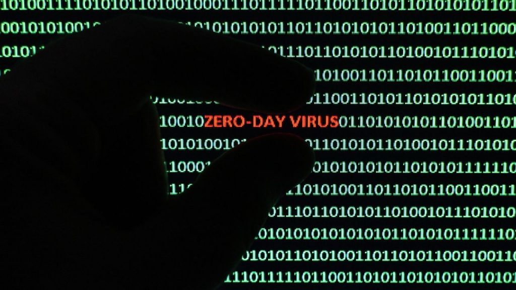 Hand highlighting the words “Zero-Day Virus” in red against binary code background.